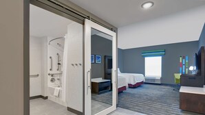 A modern hotel room with a shower, a bed, a desk, and a view of the outside. - Hampton Inn & Suites MacClenny I-10 (MacClenny)