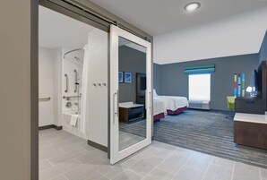 Habitación de hotel moderna con ducha, cama, escritorio y vistas al exterior.