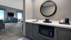 A modern kitchen with a large round mirror, a built-in microwave, and a coffee maker on the counter. - Hampton Inn & Suites MacClenny I-10 (MacClenny)