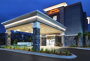 Un Hampton Inn & Suites con un área exterior cubierta, pilares de piedra y una entrada bien iluminada.