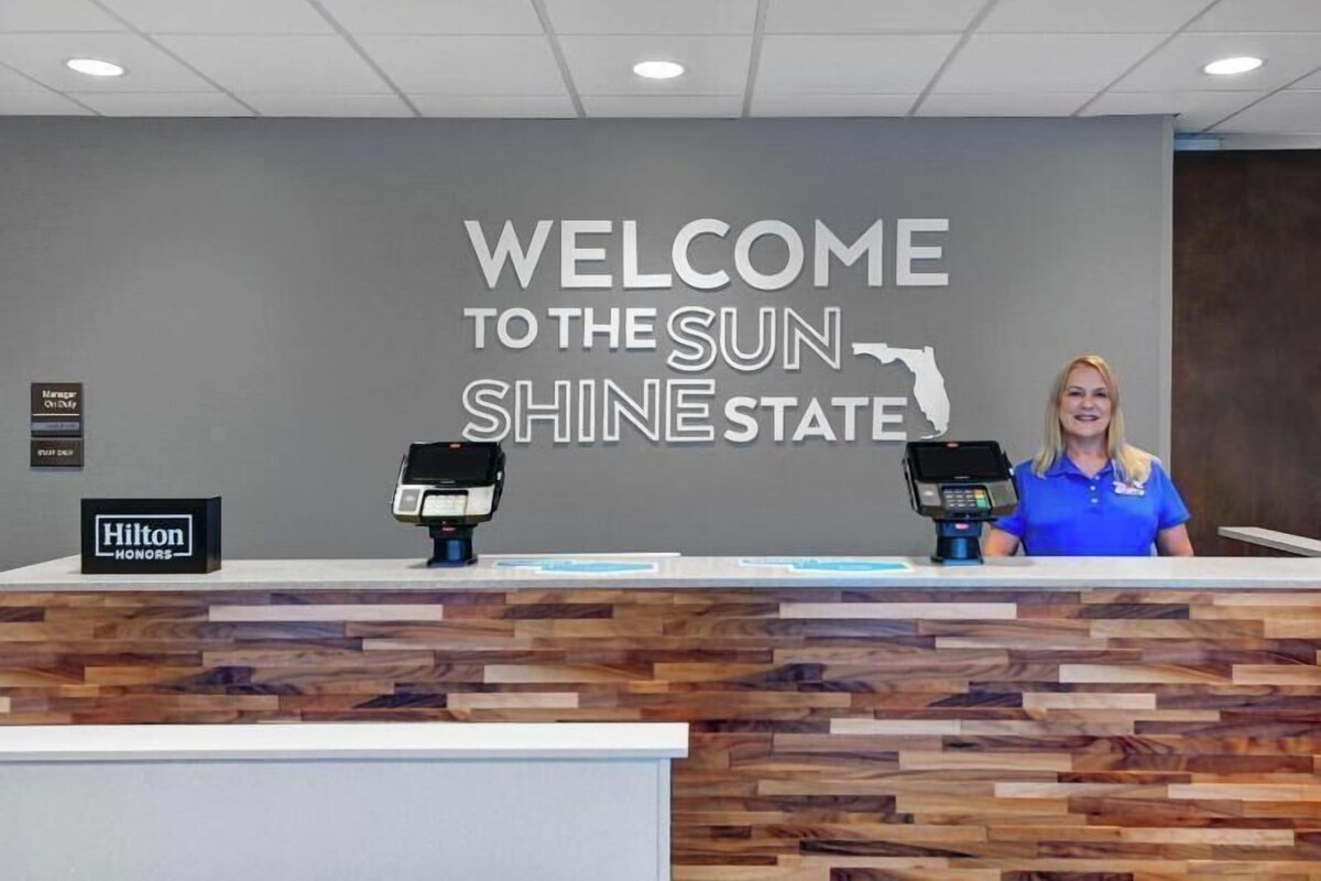 A reception desk with a 'Welcome to the Sun Shine State' sign, two card readers, and a 'Hilton Honors' sign.