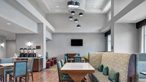 A modern hotel lobby with a dining area, seating arrangements, and a flat-screen TV mounted on the wall. - Hampton Inn & Suites MacClenny I-10 (MacClenny)