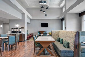 Un vestíbulo moderno de hotel con comedor, arreglos de asientos y un televisor de pantalla plana en la pared.