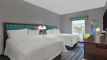 Habitación de hotel con dos camas, un escritorio, una silla, una lámpara y ventana con vistas.