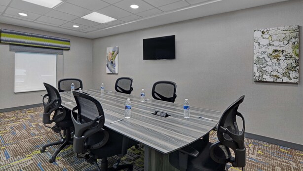 A conference room with a long table, four chairs, a projector screen, a flat-screen TV, and two water bottles. - Hampton Inn & Suites MacClenny I-10 (MacClenny)