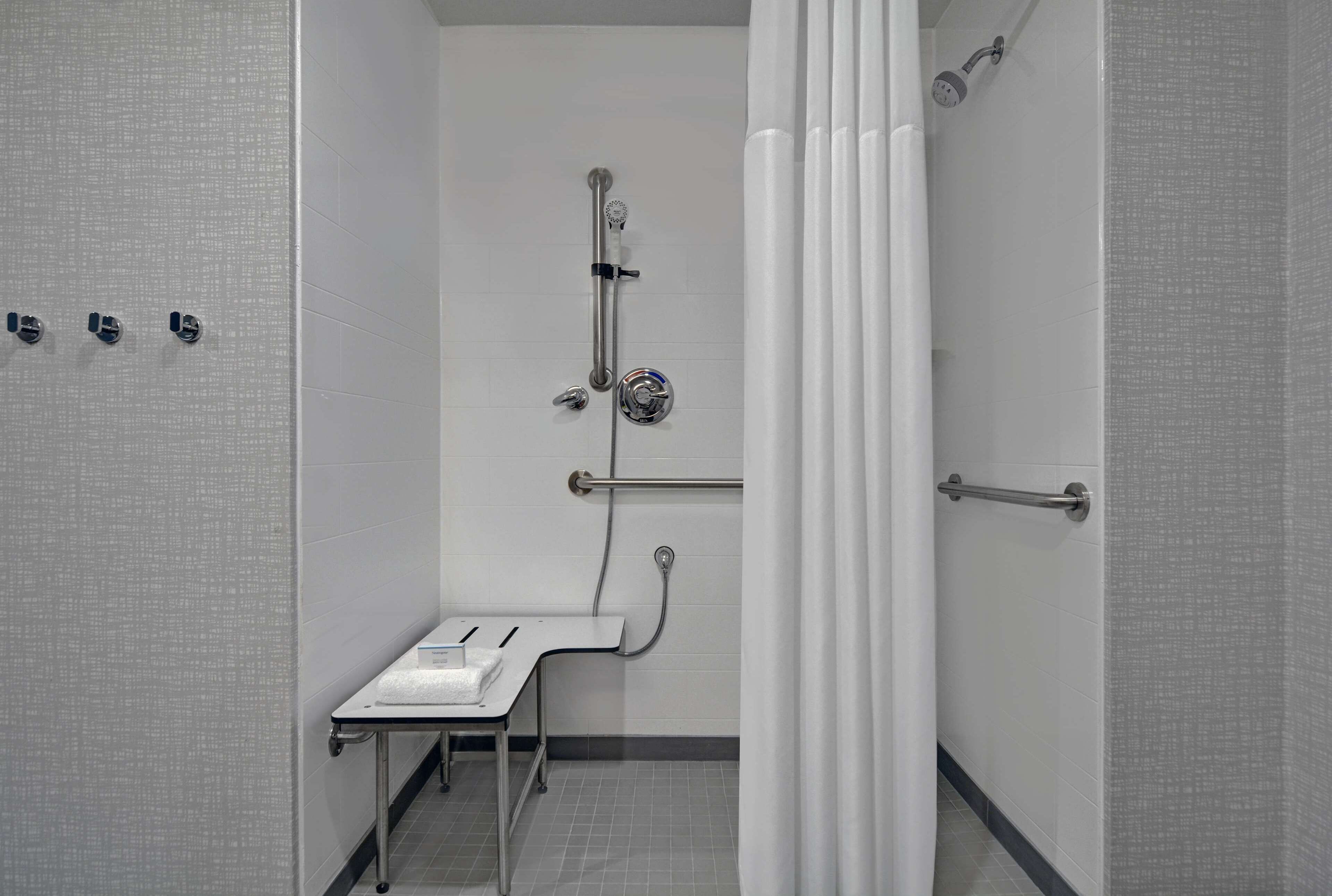 A bathroom with a shower, grab bar, and a small table with a towel.