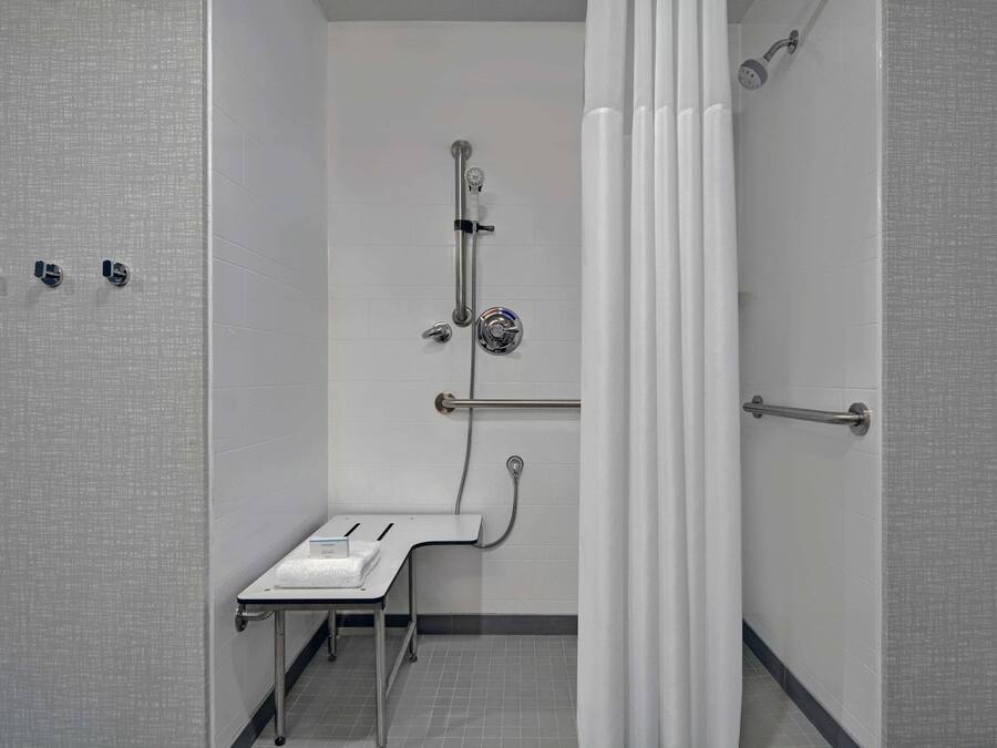 A bathroom with a shower, grab bar, and a small table with a towel.