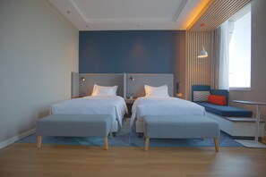 A modern hotel room with two single beds, a small sofa, and a window with curtains.