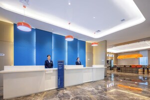 Zona de recepción de un hotel con diseño moderno, que incluye un mostrador de recepción, dos empleados y un área de descanso con mesas y sillas.