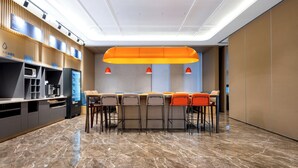Zona bar moderna con un lungo bancone, diversi sgabelli e una grande lampada arancione a sospensione.