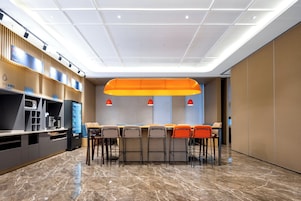 Zona de bar moderna con una barra alargada, varios taburetes y una lámpara naranja grande colgante.