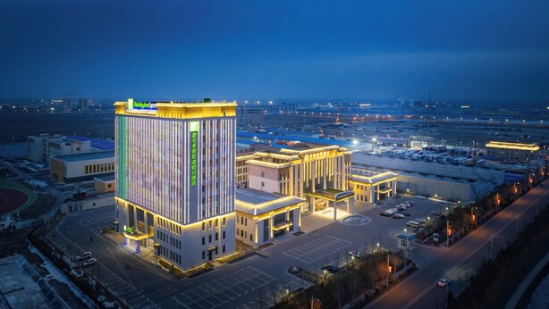 Un hotel moderno con un'imponente fascia luminosa verticale, un cortile interno e vista sulla città circostante al crepuscolo.