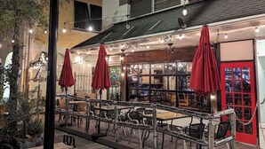 An outdoor seating area with tables and chairs, red umbrellas, and a building with a sign reading "OGGI Italian Street Chicken & Pasta". - Davis Islands Urban Fiesta 2 Bedroom (Tampa)
