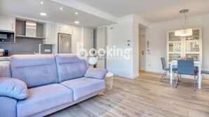 Ein modernes Wohnzimmer mit einer Couch, einem Esstisch mit Stühlen, einer Küchenzeile mit Schränken und Geräten sowie einem Flur, der in einen weiteren Raum führt.