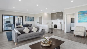Ein modernes Wohnzimmer mit einem grauen Sofa, einem Couchtisch mit floraler Dekoration und einem Essbereich mit Tisch und Stühlen.