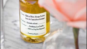 A bottle of olive oil with a label, a pink rose, and a glass on a marble surface.