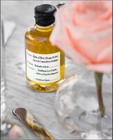 Una botella de aceite de oliva con etiqueta, una rosa rosa y un vaso sobre una superficie de mármol.
