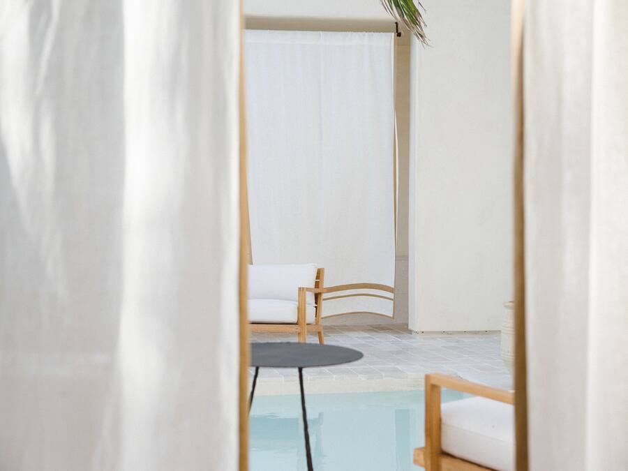 A pool area with a chair and a small table, surrounded by white walls and a curtain.