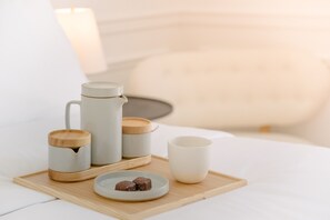 A neatly arranged breakfast tray on a bed with a white headboard, including a mug, a teapot, a cup, and a plate with two pastries. - Cara (Los Angeles)