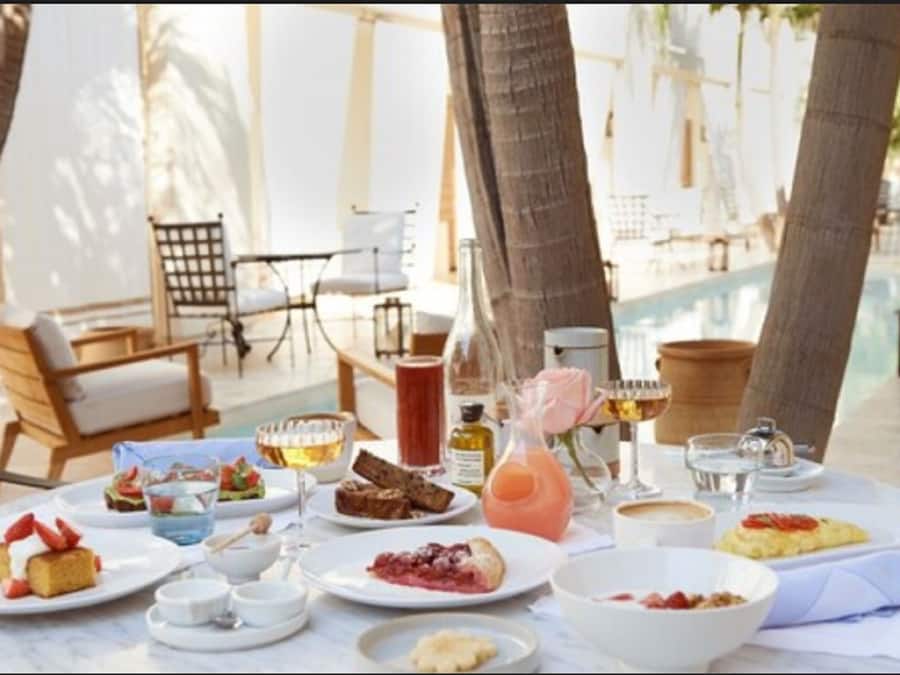Desayuno con diversos platos y bebidas sobre una mesa, rodeado de sillas y una piscina al fondo.