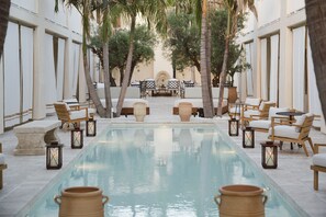 A poolside area with seating and tables, surrounded by palm trees and a building with large windows. - Cara (Los Angeles)