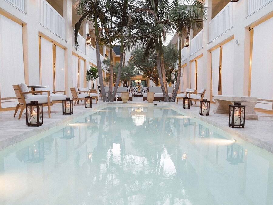 A pool area with a long rectangular pool, lounge chairs, and tables.