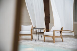 Zona piscina con due sedie di legno e un piccolo tavolino rotondo.
