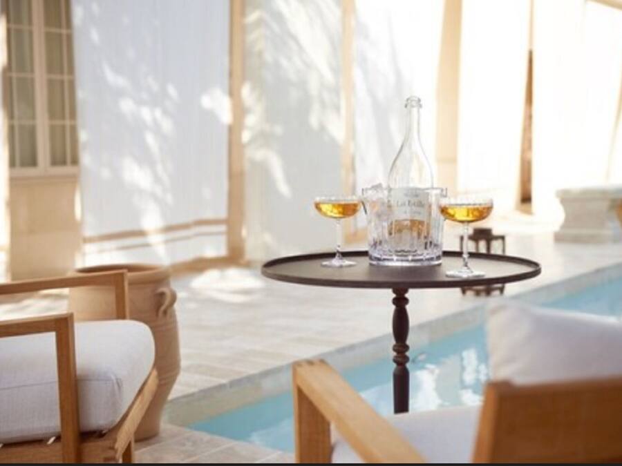 Een zwembadterras met een tafel gedekt voor twee personen, inclusief een fles en twee glaasjes.