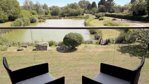 Un balcon avec deux fauteuils en osier noir donnant sur un étang et un jardin.