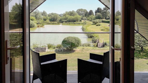 Une pièce avec deux fauteuils en osier, placés face à une grande fenêtre donnant sur un lac et une végétation luxuriante.