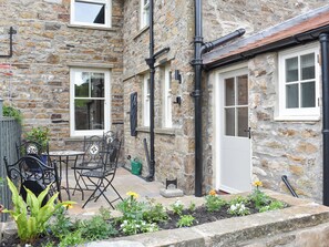 A stone building with a door, windows, and a small garden area with plants and a table. - 3 bedroom accommodation in Reeth, near Richmond (Reeth, near Richmond)