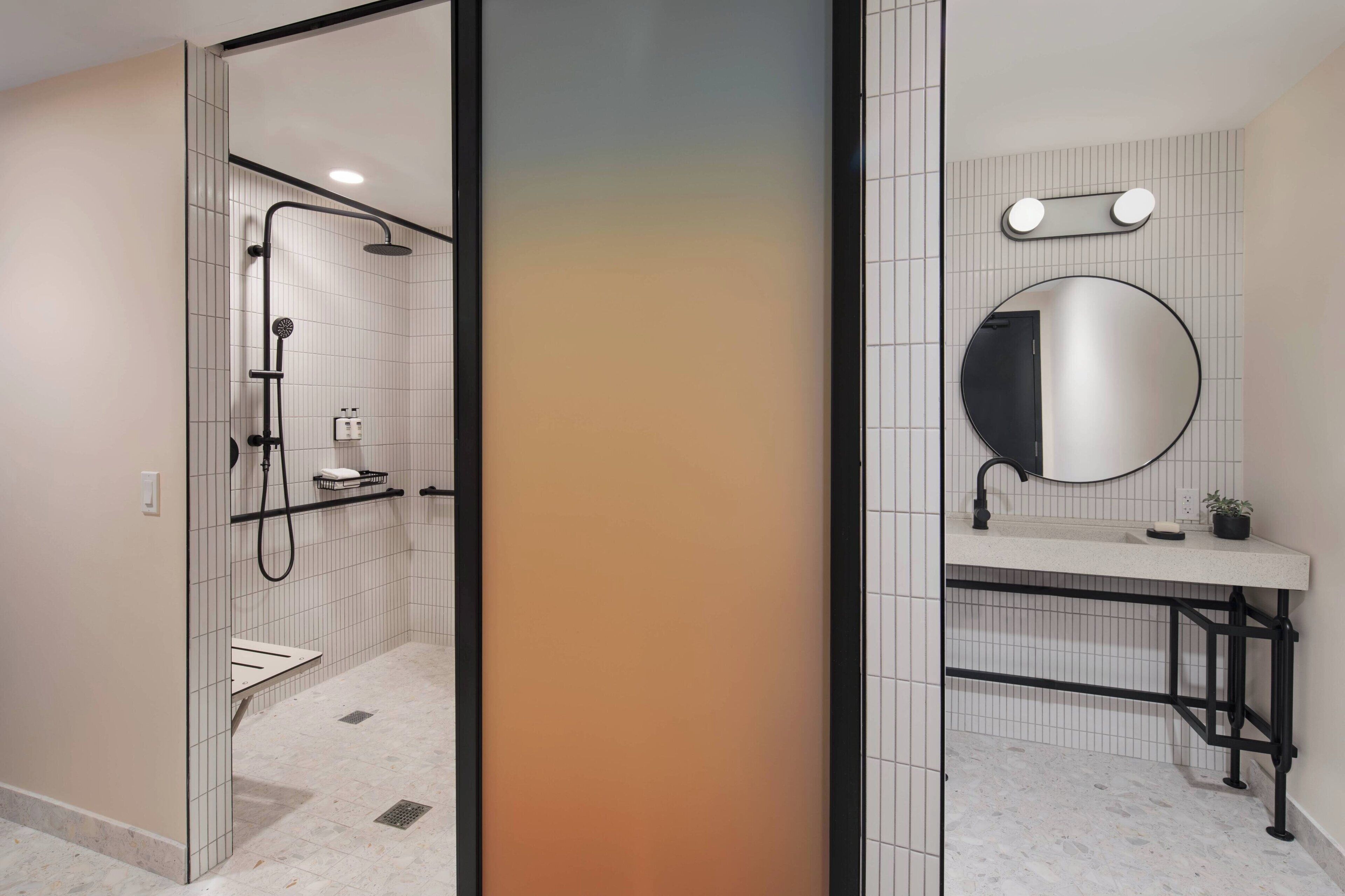 A modern bathroom with a shower, toilet, and sink, featuring a tiled wall and a round mirror.