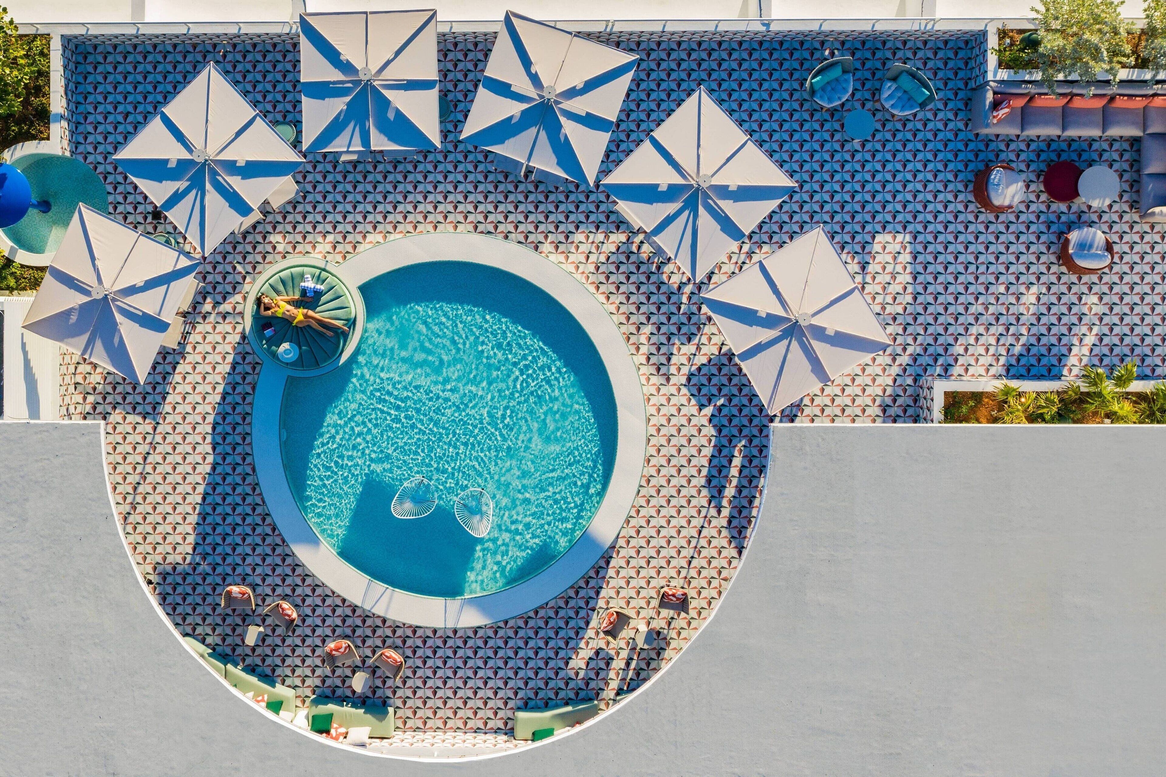 Una piscina con lettini e ombrelloni, circondata da un’area piastrellata decorata.