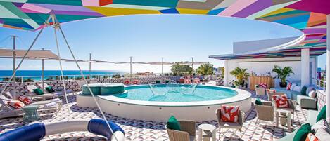 Un espace piscine doté d’un sol à motifs géométriques, de chaises longues et offrant une vue sur la mer.