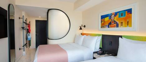 Habitación de hotel con dos camas, un espejo grande, un cuadro en la pared y una puerta que da a un pasillo.