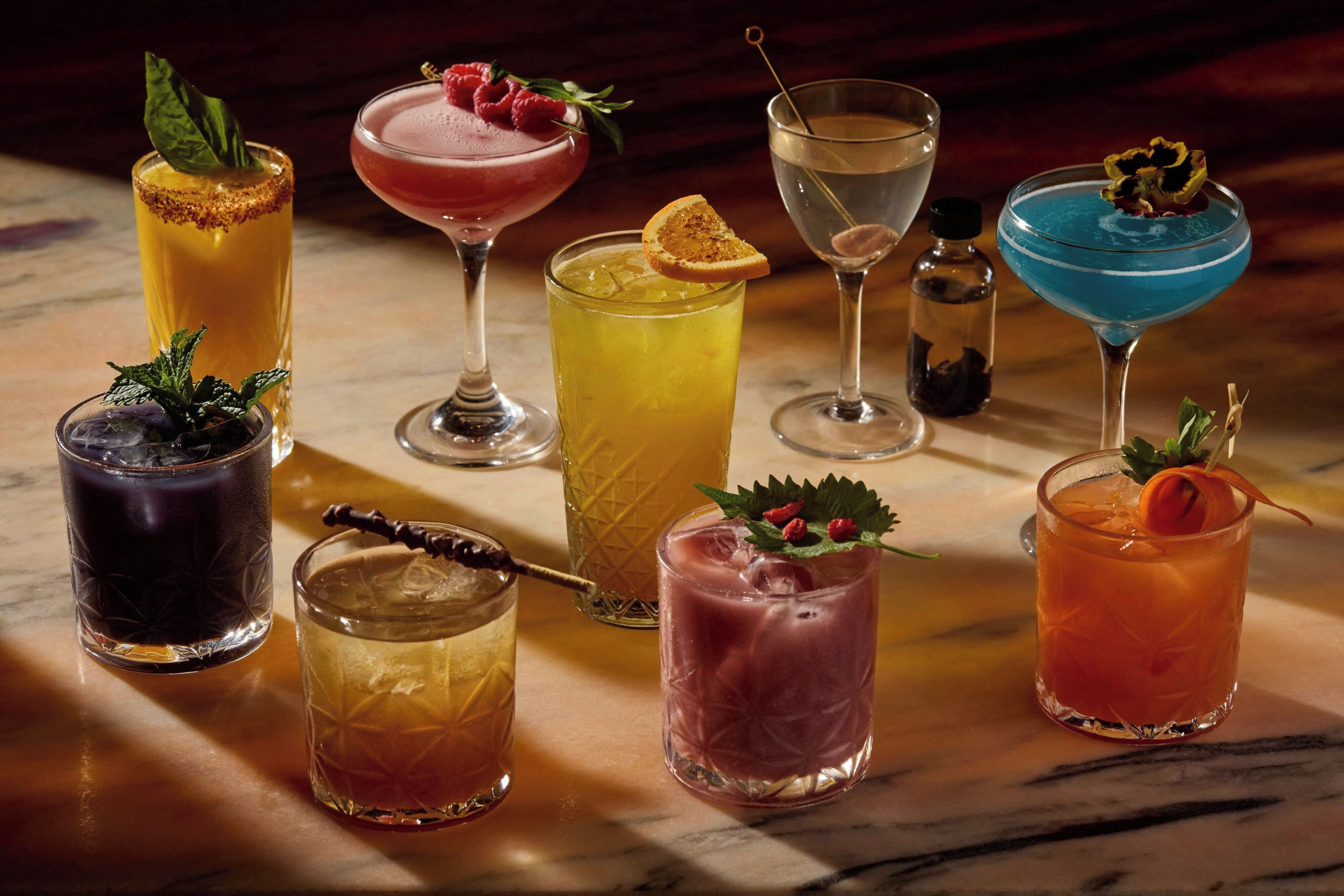 A variety of cocktails in different glassware, some with garnishes, on a marble surface.