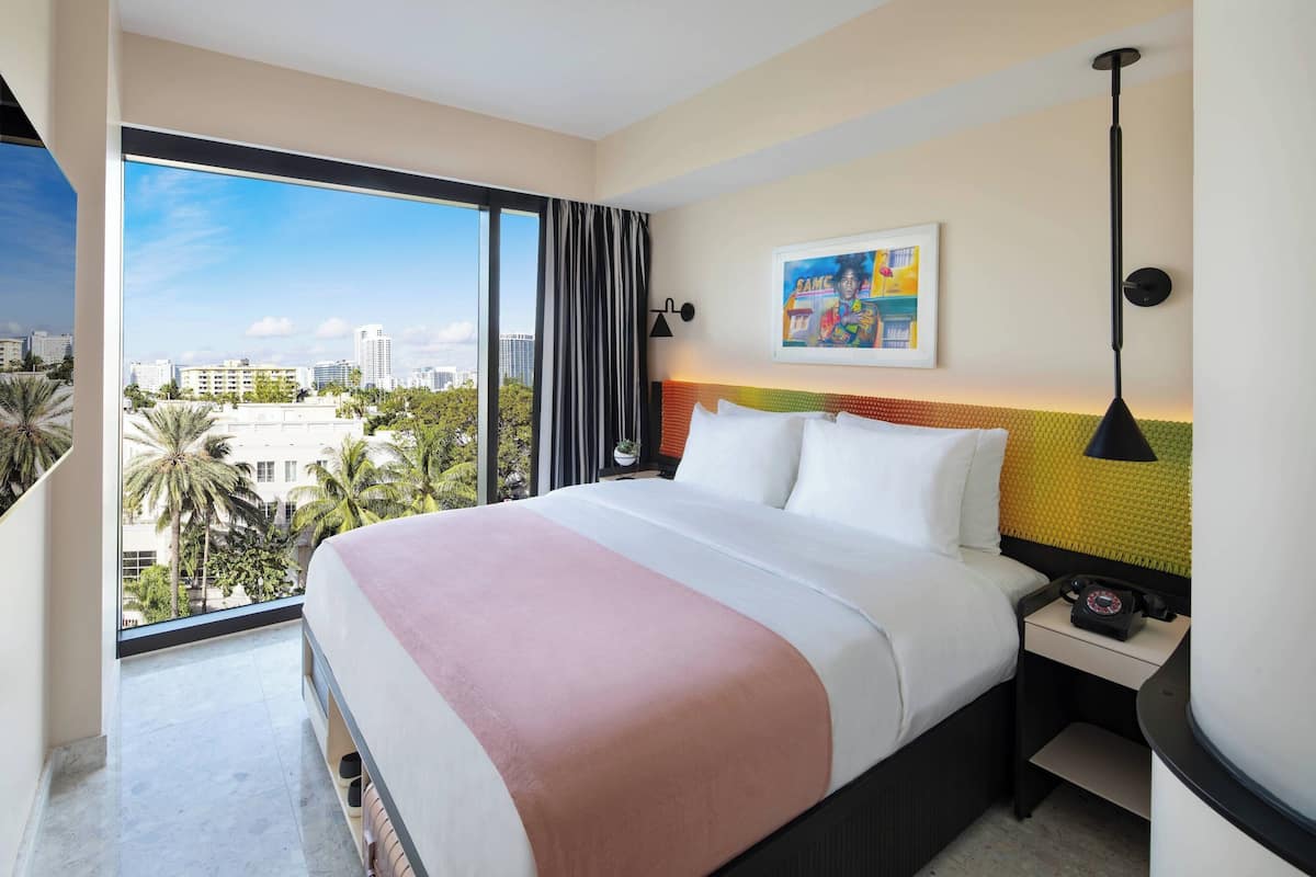 A hotel room with a large bed, a nightstand, a telephone, a wall-mounted lamp, and a painting.