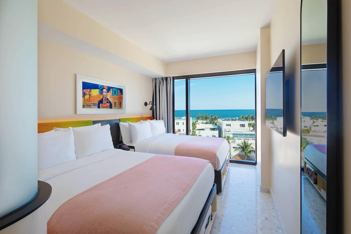 A hotel room with two beds, a large window with a city view, and a painting on the wall.
