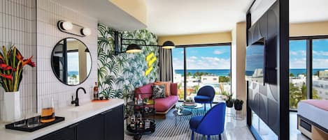 Una habitación de hotel moderna con un ventanal grande, un balcón, un sofá, una silla y un televisor.