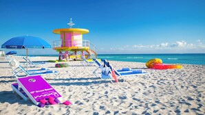 A beach with a lifeguard tower, beach chairs, umbrellas, and a sign for 10th Street Beach.
