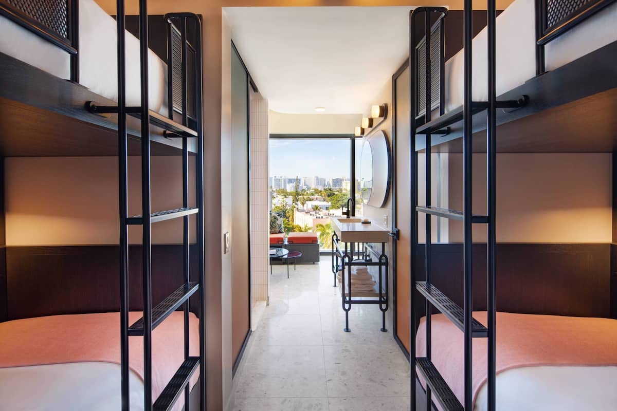A compact hotel room with bunk beds, a small dining area, and a view of the city.