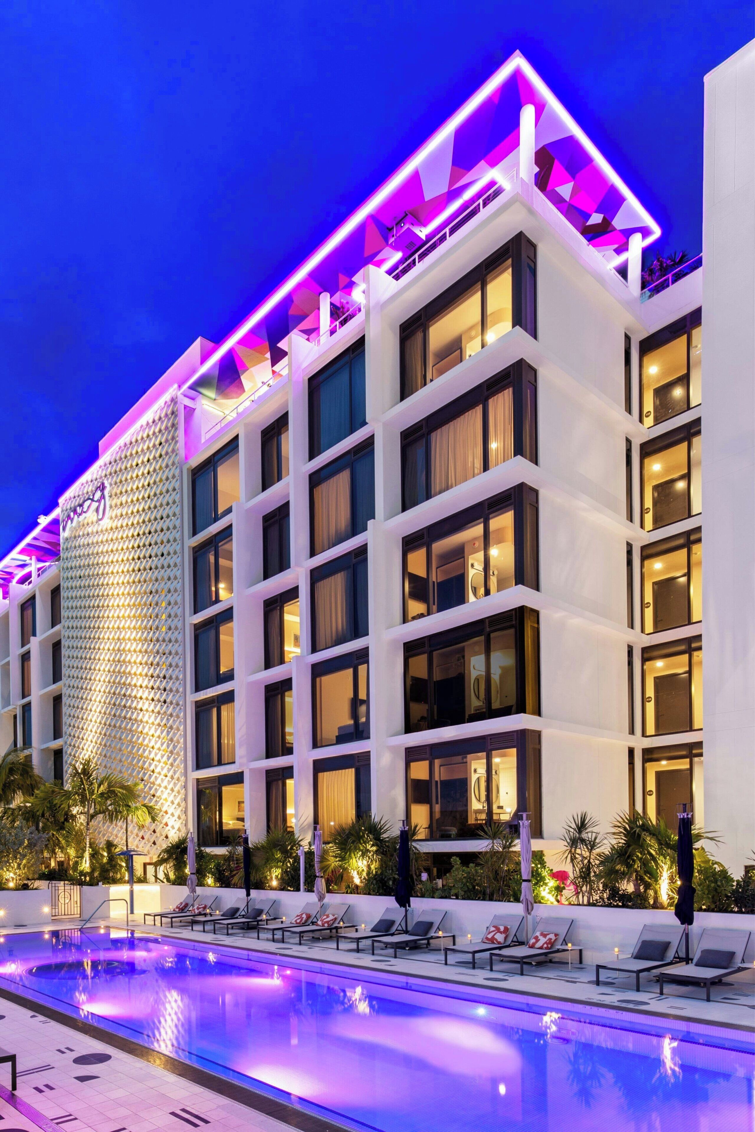 Un hotel moderno con zona de piscina, varios balcones y fachada bien iluminada.