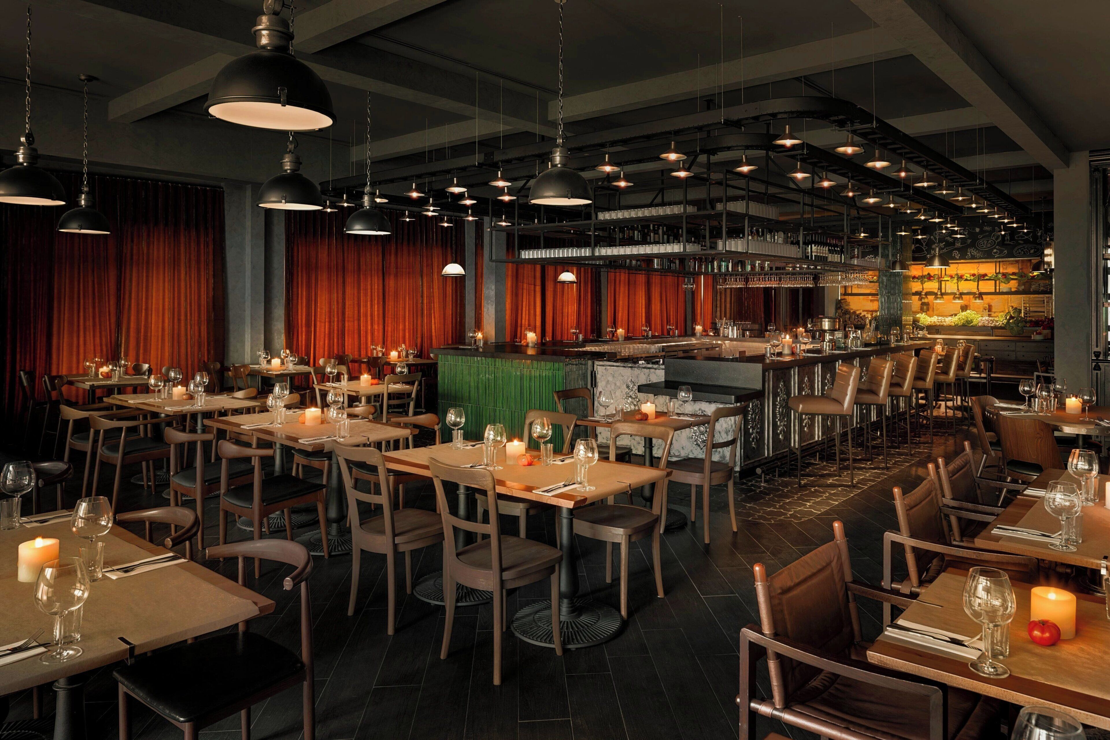 A restaurant with multiple tables, chairs, hanging pendant lights, and a bar area.