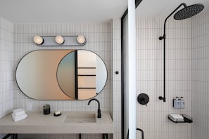 A modern bathroom with a large mirror, a sink, a shower, and a towel rack.
