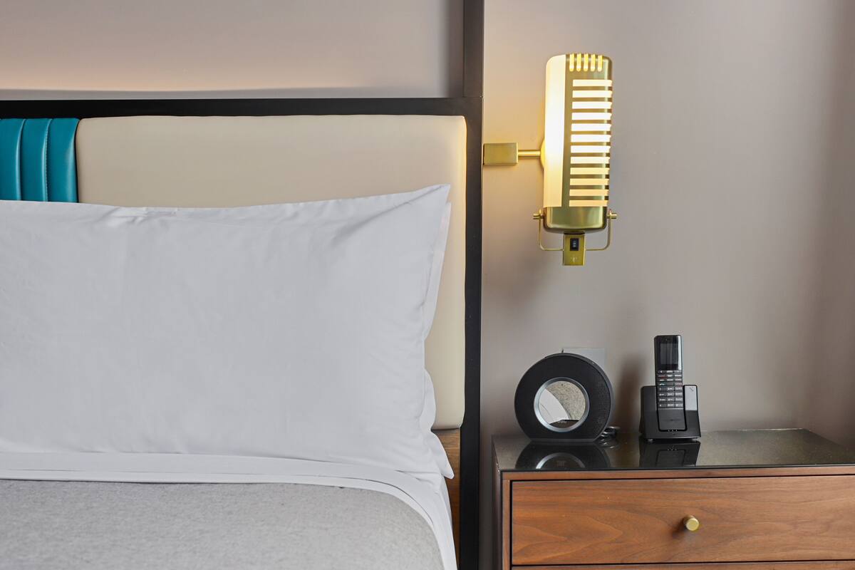 Une chambre d’hôtel avec un lit, une table de chevet avec une lampe, une horloge et un téléphone.