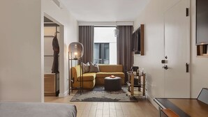 A compact hotel room with a sofa, a round ottoman, a side table, a lamp, and a TV mounted on the wall. - Canopy by Hilton Memphis Downtown (Memphis)