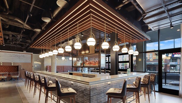 A modern bar area with a central island, bar stools, pendant lighting, and a view of the city through large windows. - Canopy by Hilton Memphis Downtown (Memphis)