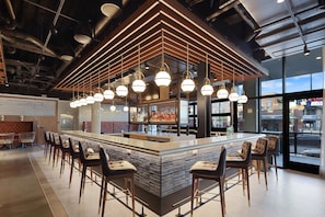 A modern bar area with a central island, bar stools, pendant lighting, and a view of the city through large windows.