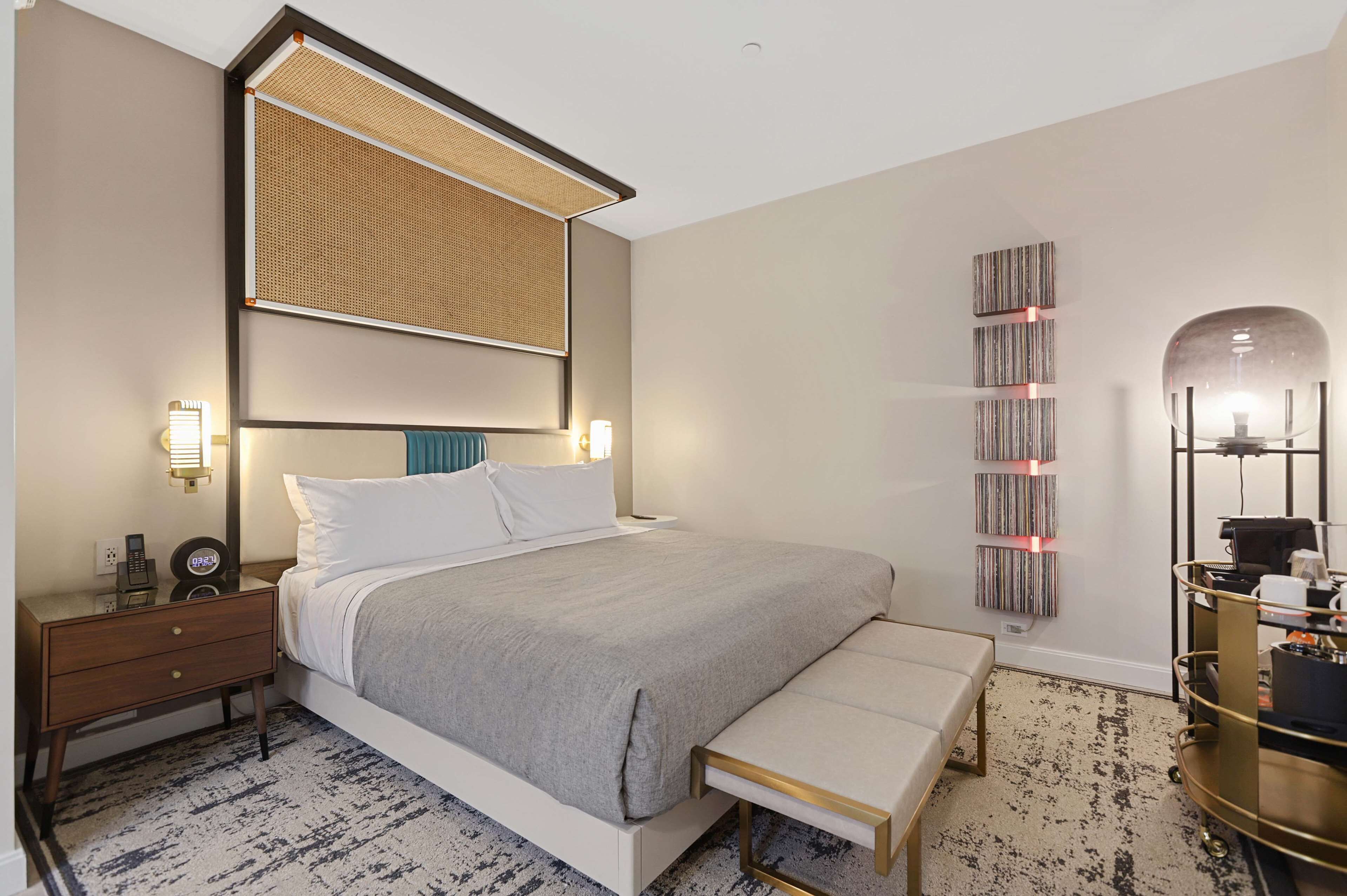 Een moderne hotelkamer met een groot bed, nachtkastje en een klein bureau met lamp.