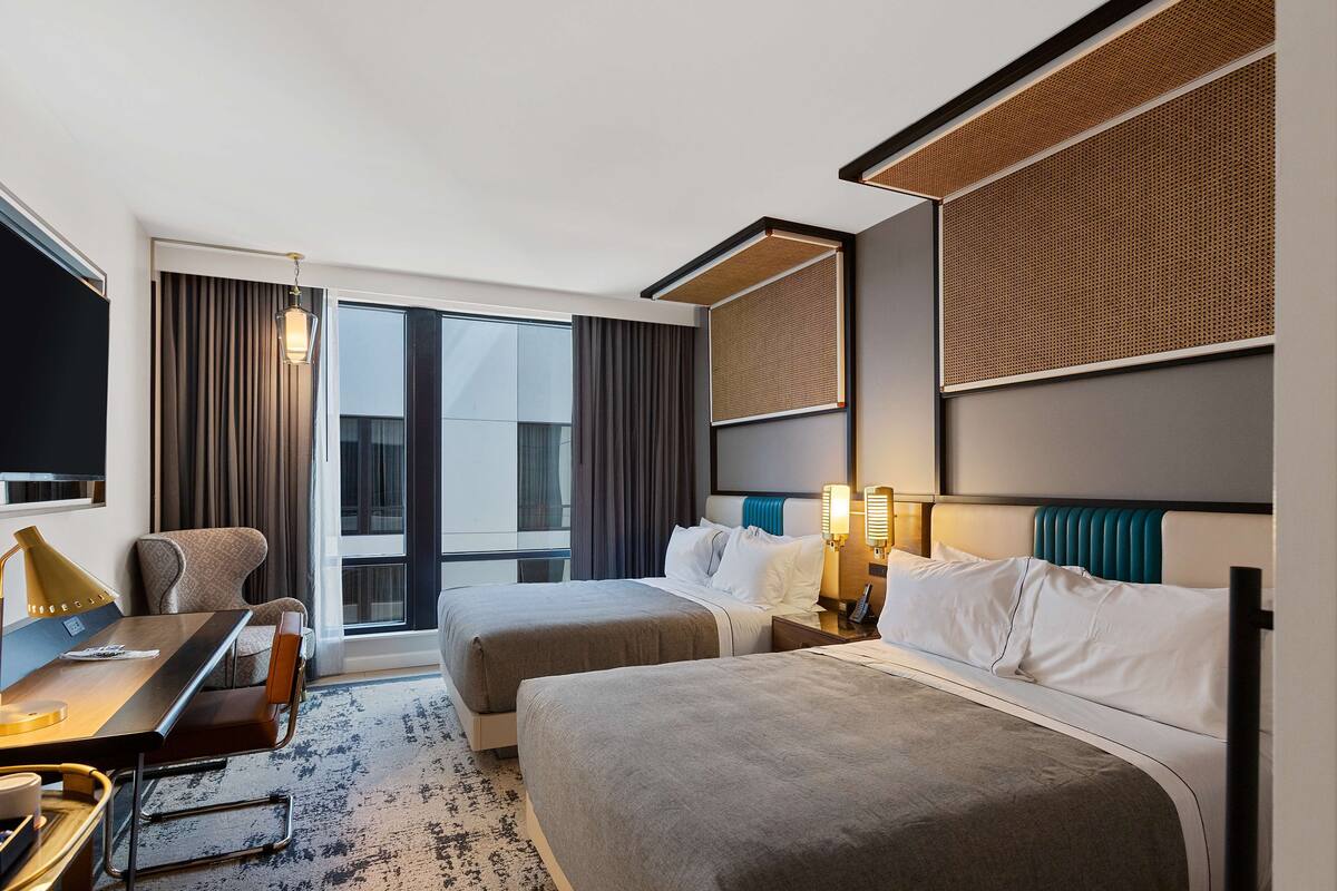 Une chambre d’hôtel avec deux lits, un bureau, une chaise, une télévision et une grande fenêtre.